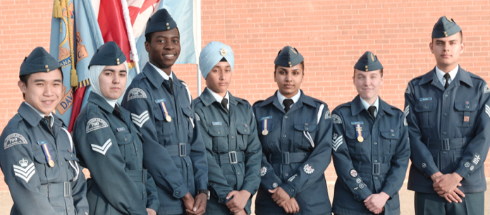 A group of Air Cadets in uniform, standing in a line, in front of flags.